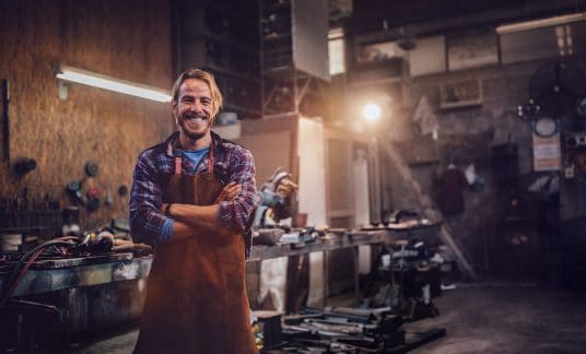 Happy professional craftsman standing in workshop with tools