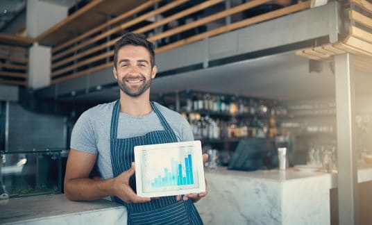 Portrait of a young man holding a digital tablet with a graph on the screen at a coffee shop