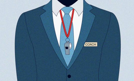 Trunk of a person wearing a blue suit and tie with a name tag that says “Coach” and a whistle around the neck.