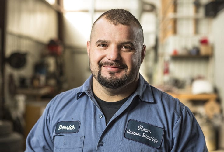 Derrick Olson wearing a blue button-down shirt with patches showing his name and business name