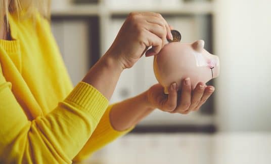 Woman wearing a yellow shirt is putting a coin into a piggy bank