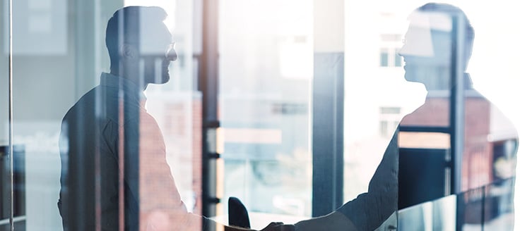 A man’s reflection is visible in the glass office door he’s about to open. A certificate of good standing is helpful if you want to acquire or sell a business.