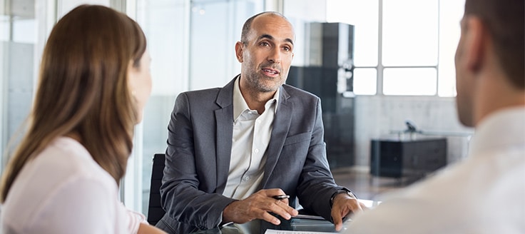 Three people sit down for a business meeting in an office.