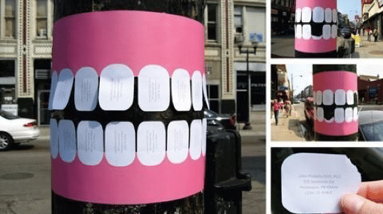 A pretend mouth on a light pole in a city; a guerilla marketing strategy. Each fake tooth can be removed by prospective customers.