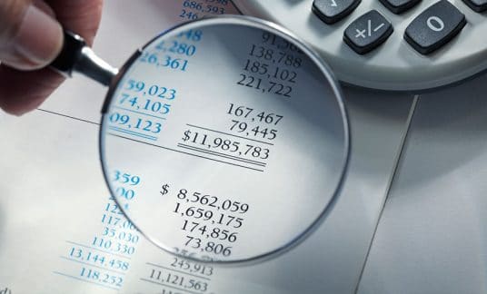 A magnifying glass hovers over numbers on a balance sheet. Learn the relationship between assets, liabilities and equity.