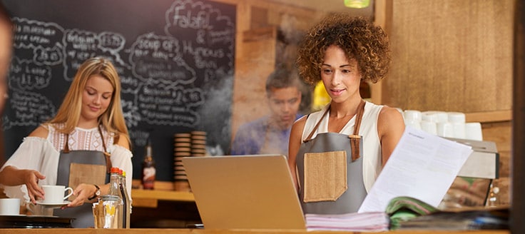 A cafe owner works on her laptop from her shop. She might be checking the balance in her business bank account.