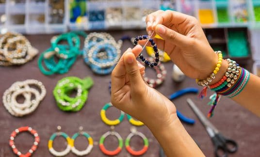 Woman creating a handmade bracelet to sell on an Etsy competitor site. 