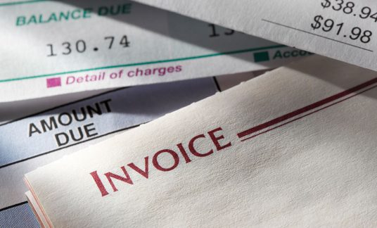 An array of invoices sit on a desk. Find the best invoice software for small business.