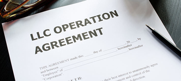 An LLC operation agreement document is placed on a desk near a pair of glasses and a pen. You might have to file an operating agreement with your articles of organization.