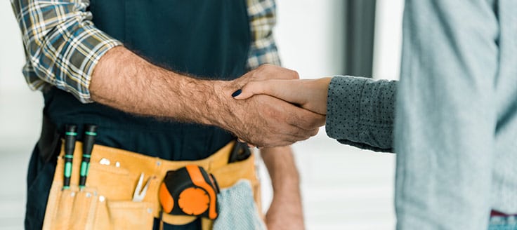 A home repair specialist, seen with his toolbelt, shakes hands with a homeowner after completing a job.