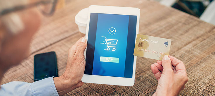 A man holds his credit card as he makes a purchase on his tablet.