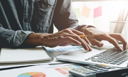 Accountant holding pen working on laptop, using a software alternative to QuickBooks 