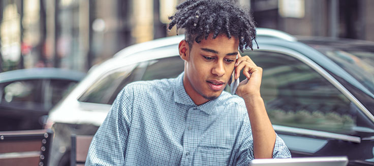 A young man looks at his laptop screen and talks on his smartphone. He could be getting interviewed for a position he found on a free job posting site.