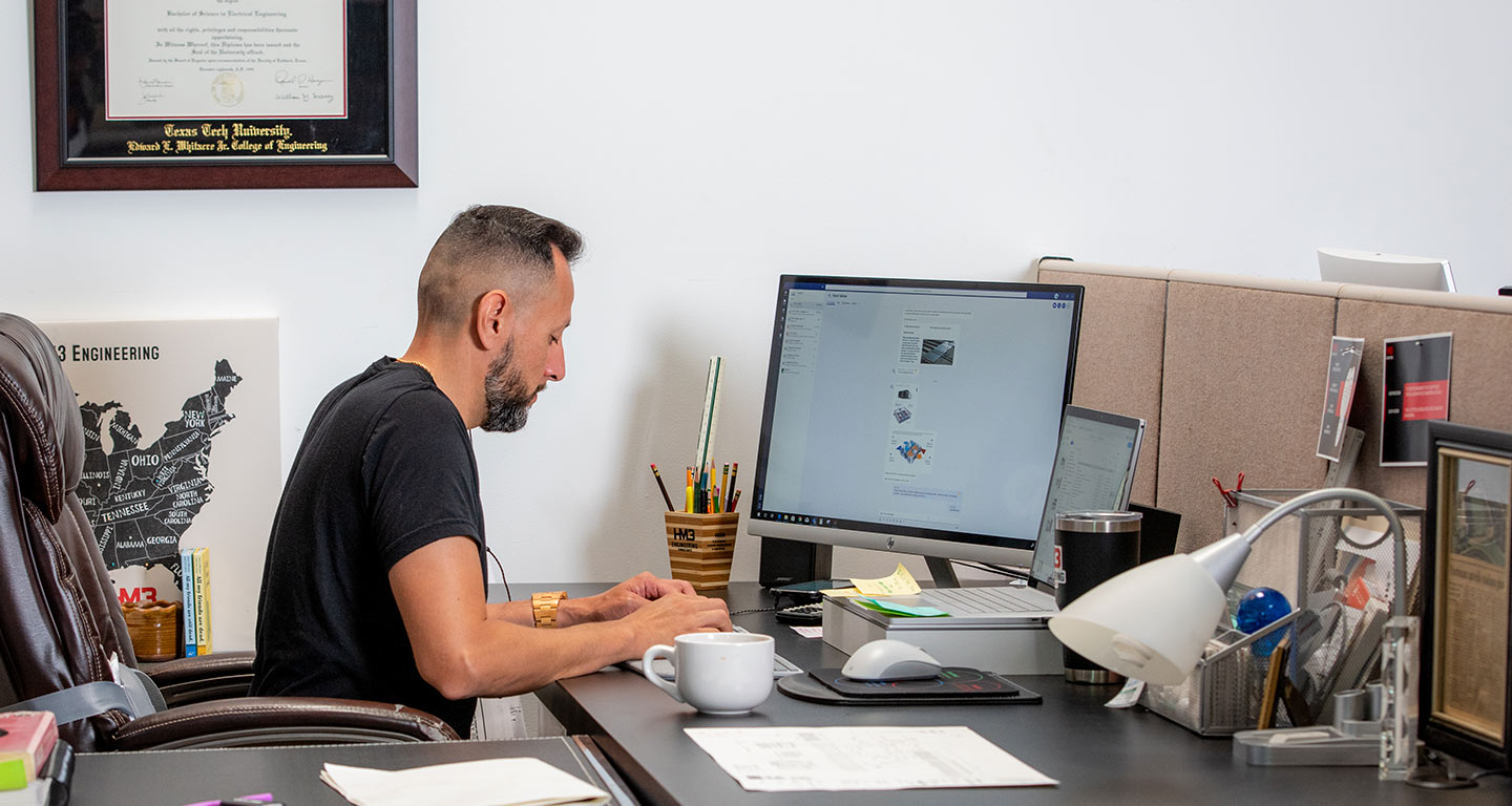 Alfred Hernandez typing on his keyword at his desk