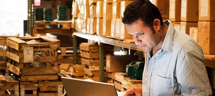 Man in warehouse looking at PC while calculating the value of a company.