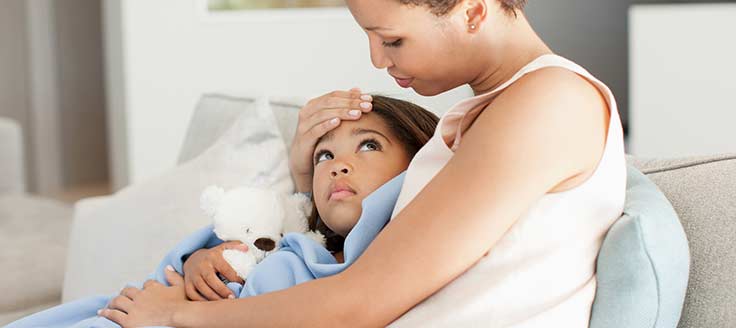 A woman holds her sick child as they sit together on a couch. California paid sick leave law allows employees to take paid sick leave to care for an ill child or another family member.