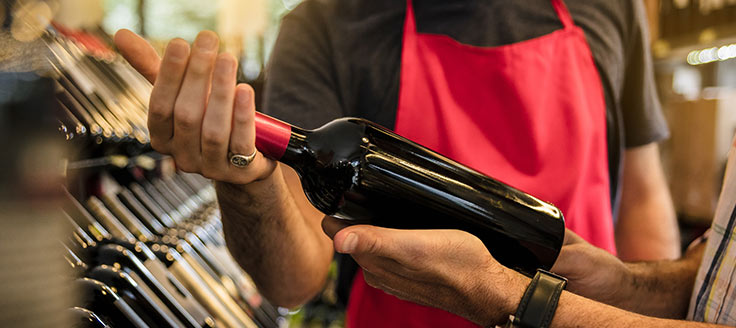 A liquor shop employee hands a wine bottle to a customer.
