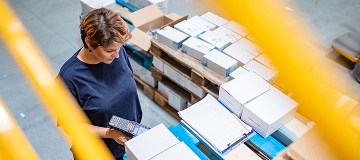 A woman scans packages in a warehouse as they prepare for shipping.