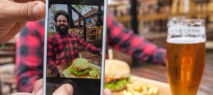 A man poses with his plate of food and beer as he enjoys a meal at a restaurant. User-generated content is a great tool for your social media promotions.