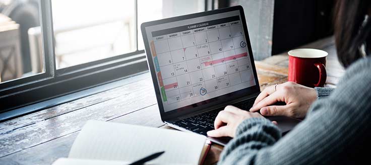 A businesswoman works at her desk on her laptop as she views the appointments she’s made with free booking software.