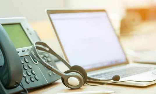 Close up of a business virtual phone number system and headset sitting on a desk. 