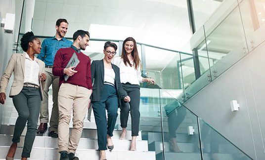 Several male and female co-workers walk down the stairs together. Business casual attire is acceptable in many industries and positions. 