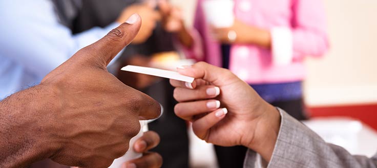 A businesswoman hands her business card to a man at a networking event.