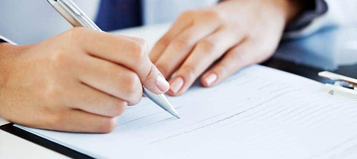 A person holds a pen and signs a paper, which could be an employment agreement.