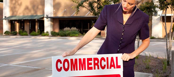 A real estate agent puts a sign in front of a commercial property.