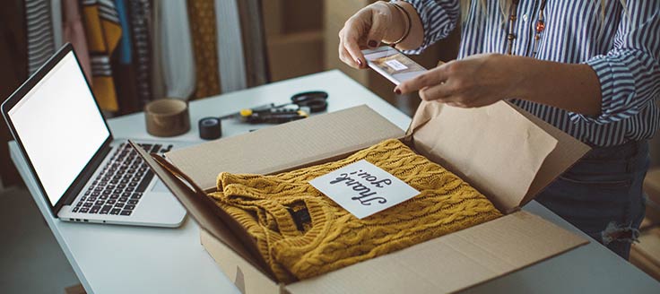 Woman, owner of a small business, is packing products in boxes, preparing them for delivery.