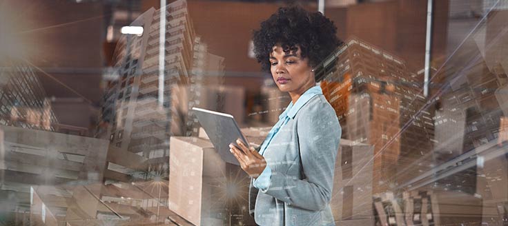 A businesswoman stands in a warehouse, surrounded by boxes of inventory.