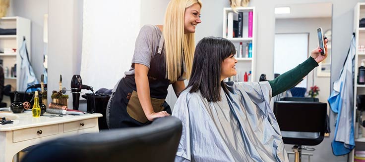 A woman takes a selfie with her hairstylist, showing off her new haircut. Emphasizing customer experience is a big business trend in 2020.