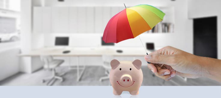 An umbrella representing business insurance held over a piggy bank.