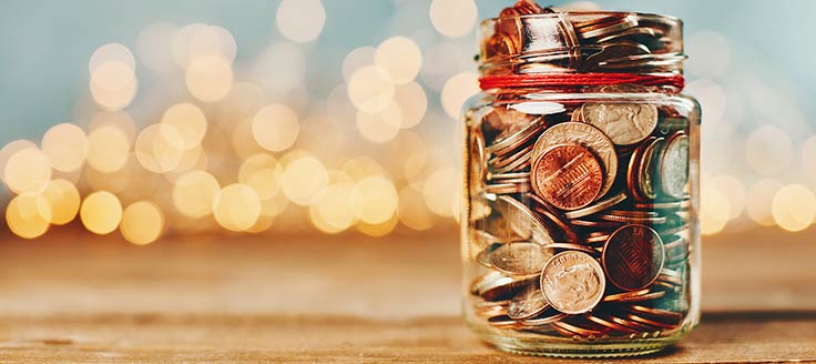 A jar filled with coins set in front of holiday lights. Don’t overspend when you own multiple businesses.