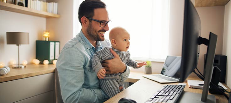 A father holds his baby as he works from home.