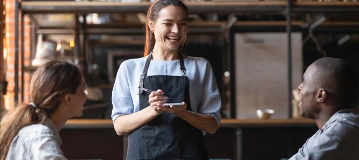 A waitress smiles at a couple she is serving at a restaurant. Being positive is a way to calm an upset customer.