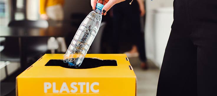 A woman places a plastic bottle in a recycling bin.