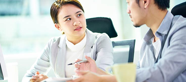 A businesswoman and businessman talk in an office. You can craft or download your own employee performance review template.