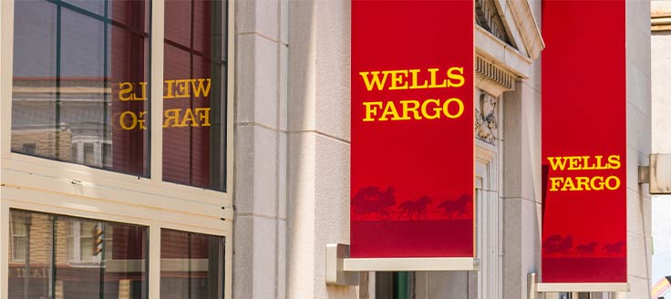 Exterior of a Wells Fargo bank, with red banners hanging outside featuring the bank logo.