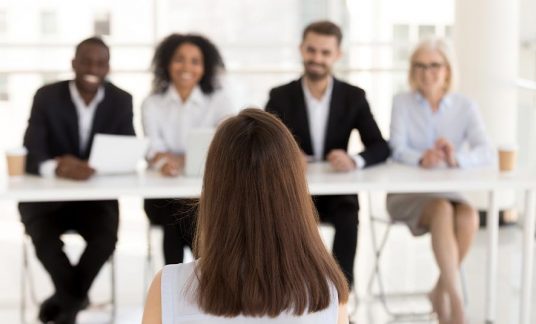 A job candidate recommended by a staffing agency sits before a panel of interviewers.