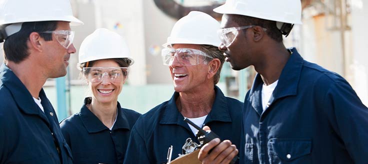Uniformed workers wear protective goggles and hard hats while out at a job site.