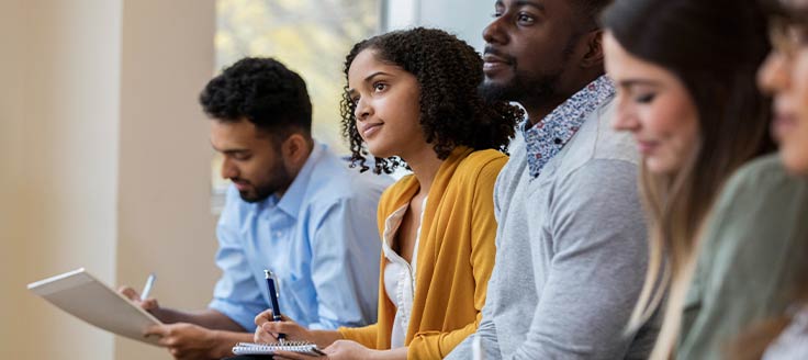 A group of people listen to a speaker or presentation and take notes. HR can handle training for employee advancement.