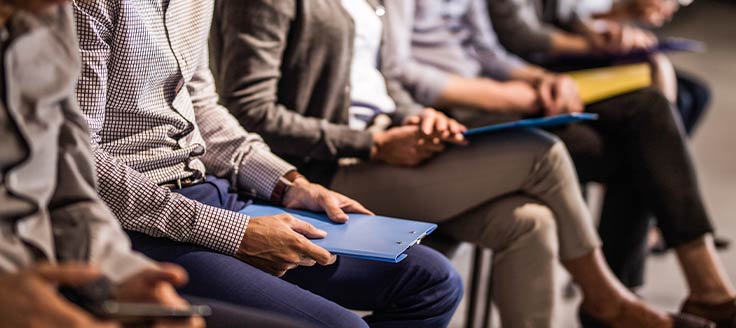 People sit in a row of chairs as they wait to be interviewed. Know the latest employment law changes to keep your business in good standing.