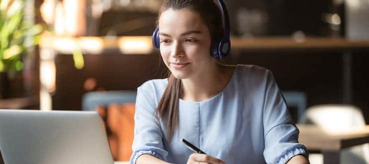 A young woman uses headphones to listen to one of the 9 best business podcasts.