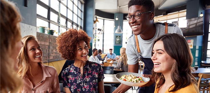 A young man delivers a food bowl to a table of restaurant patrons. Good customer service key to overall customer experience.