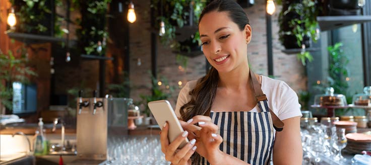A woman works on her mobile phone at her restaurant. A good mobile website or app is important to customer experience.