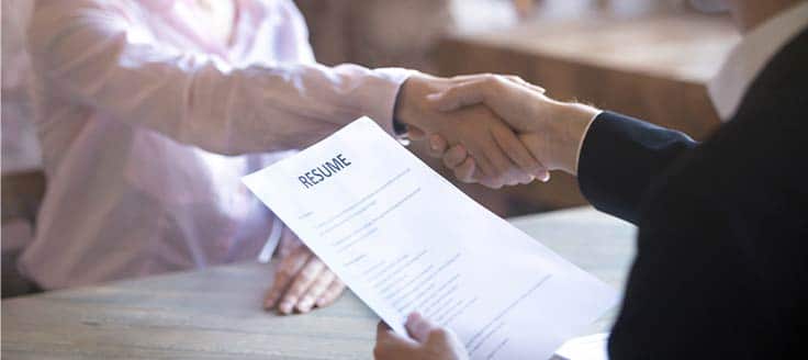 A hiring manager shakes hands with a job candidate as they accept the person's resume.