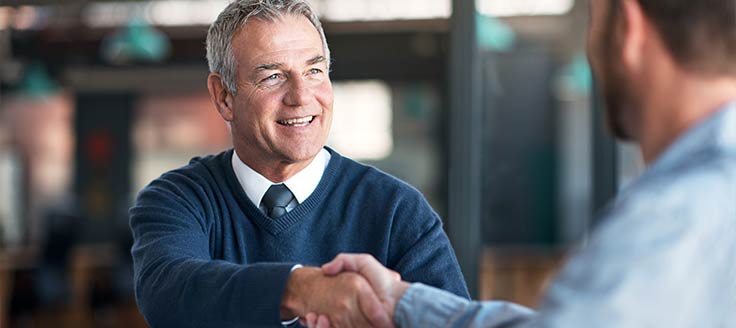 Two men shake hands in a business office. It's important to consider stakeholders when making a business succession plan.
