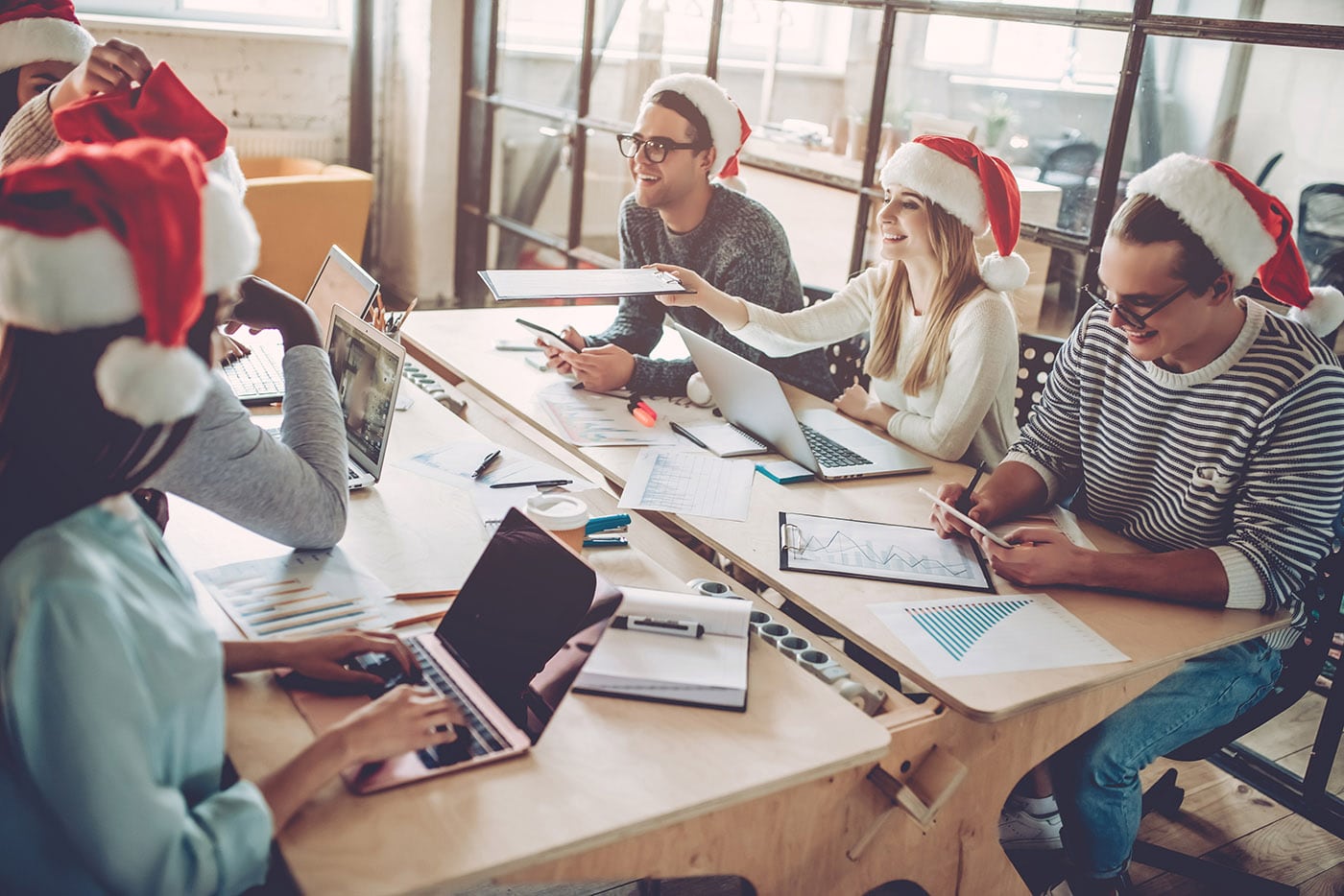 Office workers wearing Santa hats are having a casual meeting and are seated at a table