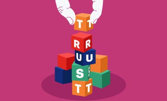 Building block form the word “Trust” with a hand adding the final block.